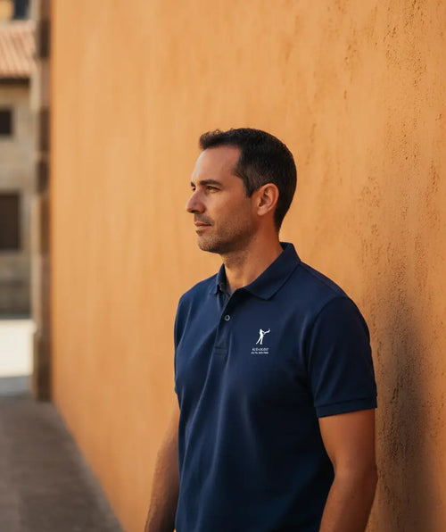 Homme portant le polo Pelote Basque bleu marine devant un mur ocre de fronton de pelote basque