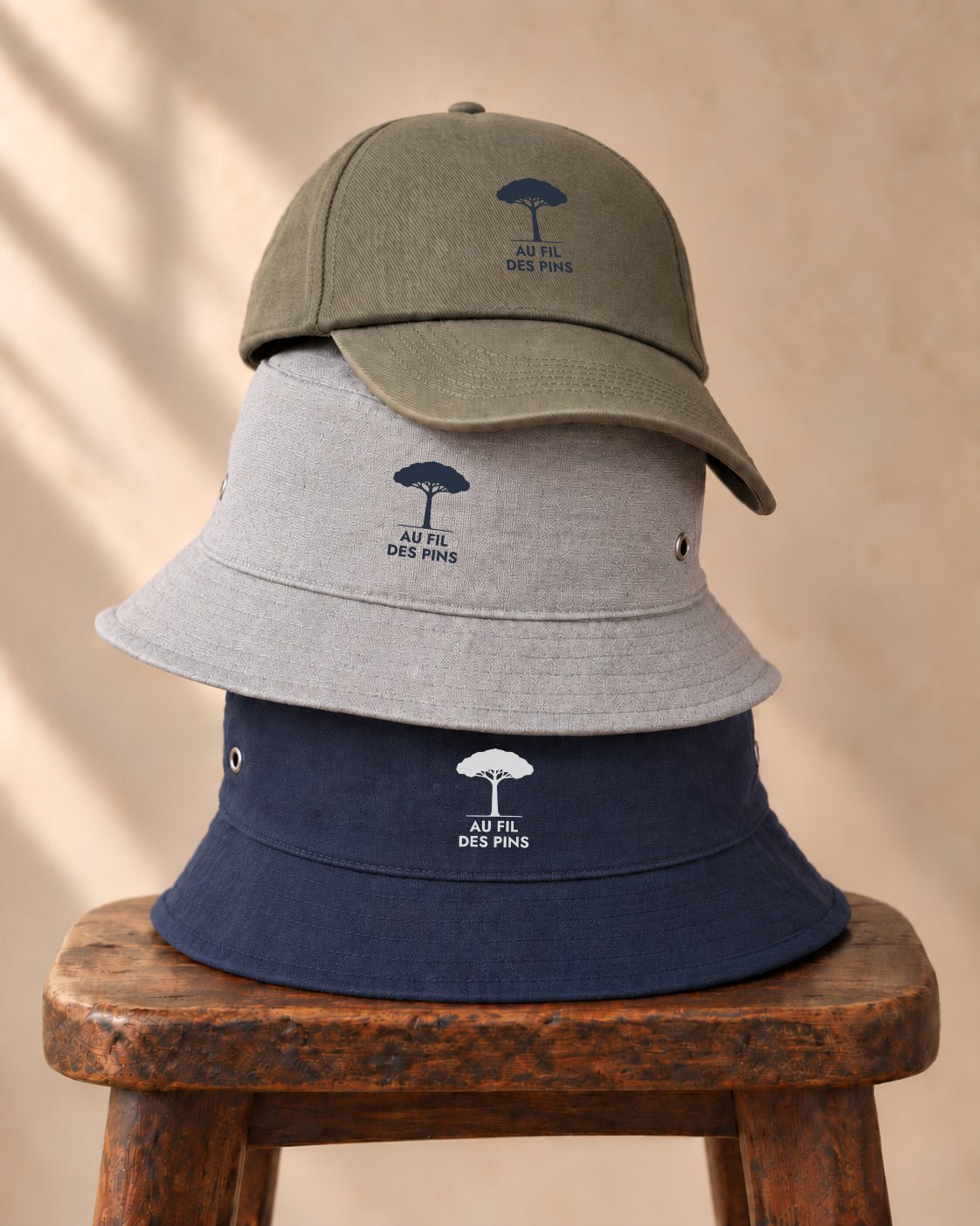 une pile de bobs gris et l'autre marine, surmontée d'une casquette kakie, le tout posés sur un tabouret en bois brut