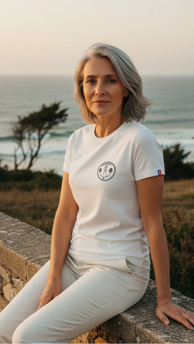 Femme en t-shirt blanc Échassier Landais Made in France assise face à l'océan au coucher du soleil – Au Fil des Pins