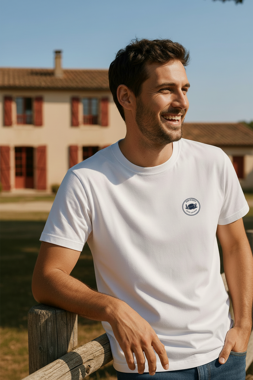 homme portant un t-shirt blanc avec badge rugby, devant une maison du sud-ouest
